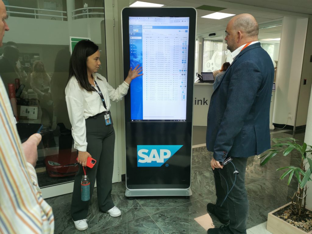 Frau steht vor SAP Stele und erklärt darauf angezeigte Daten