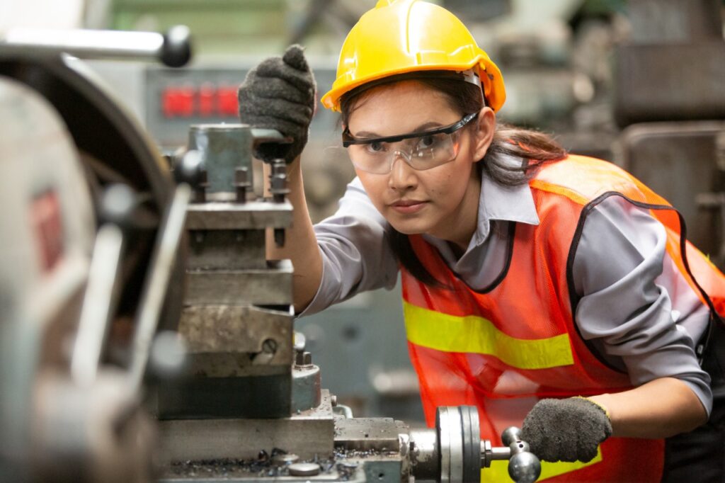 Junge Frau mit Schutzhelm arbeitet an einer Maschine.