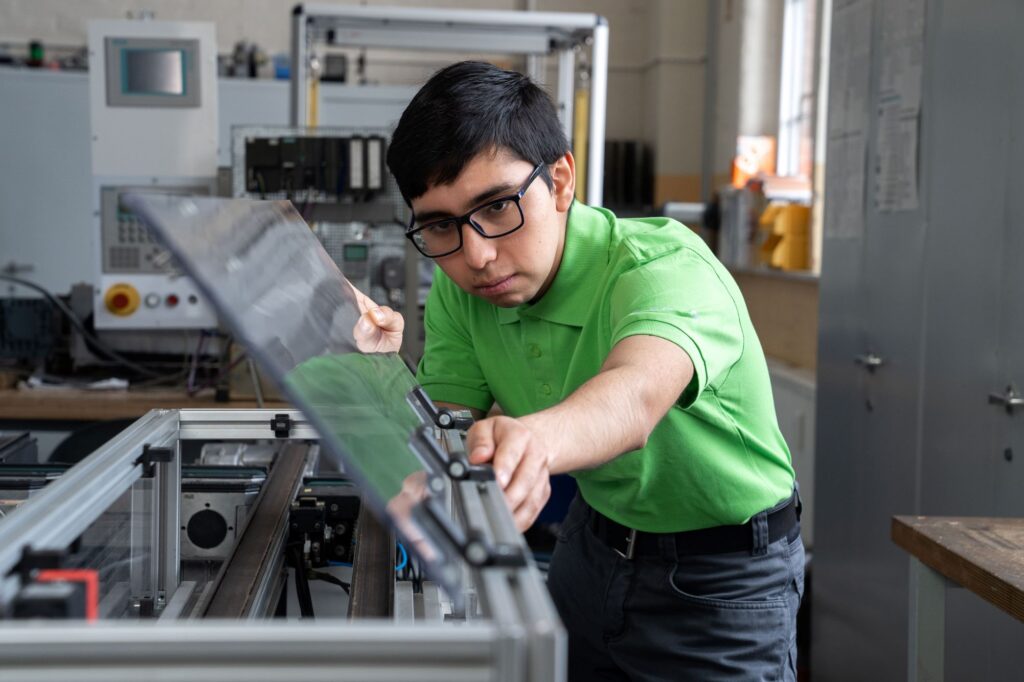 Junge aus Chile arbeitet an einer Maschine mit Glas.